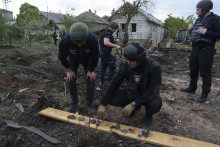Ukrajinský policajt a prokurátor pre vojnové zločiny si prezerajú úlomky bomby pred poškodeným domom po ruskom ostreľovaní obytných častí východoukrajinskeho mesta Charkov. FOTO: TASR/AP