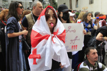 Demonštrantka zahalená v gruzínskej národnej vlajke stojí pred políciou počas opozičného protestu proti návrhu zákona o zahraničnom vplyve pred budovou parlamentu v Tbilisi. FOTO: TASR/AP