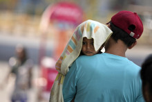 Muž nesie dieťa s hlavou prikrytou uterákom, aby ho chránil pred horúčavou v indickom Džammú. FOTO: TASR/AP