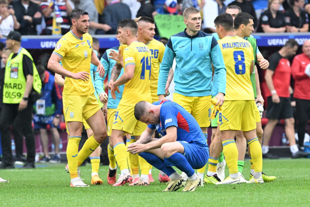 Ukrajinskí futbalisti oslavujú, vpredu dole je smutný Milan Škriniar (Slovensko) po zápase základnej E-skupiny Slovensko - Ukrajina na ME 2024. FOTO: TASR/Martin Baumann