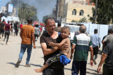 Muž nesie dieťa na mieste, kde podľa Palestínčanov došlo k izraelskému útoku v stanovom tábore v oblasti Al-Mawasi.  FOTO: Reuters