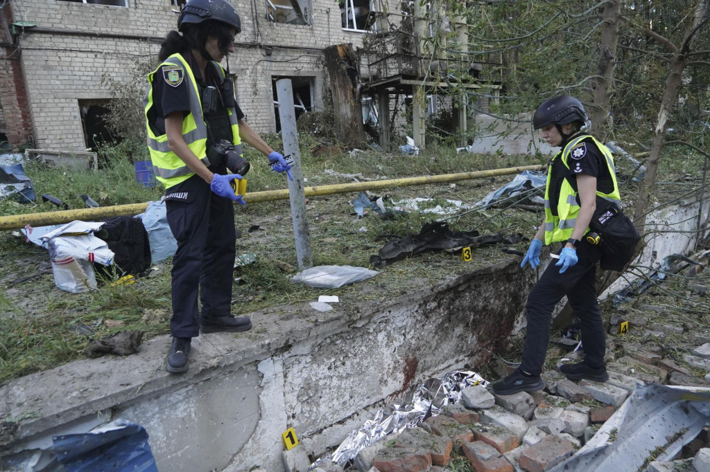 Policajti dokumentujú dôkazy pri tele muža, ktorý zahynul pri ruskom útoku na mesto Charkov. FOTO TASR/AP