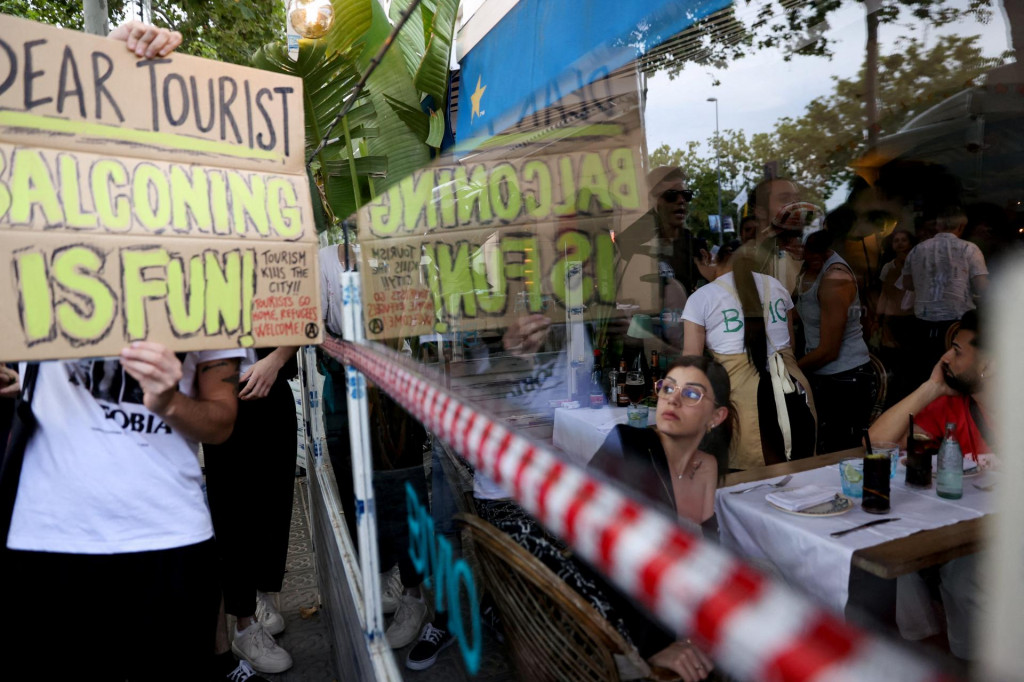 Turista sleduje, ako demonštranti protestujú proti masovému turizmu v Barcelone. Katalánska metropola prijala v roku 2023 viac ako 12 miliónov turistov a v roku 2024 ich očakáva ešte viac. FOTO: REUTERS