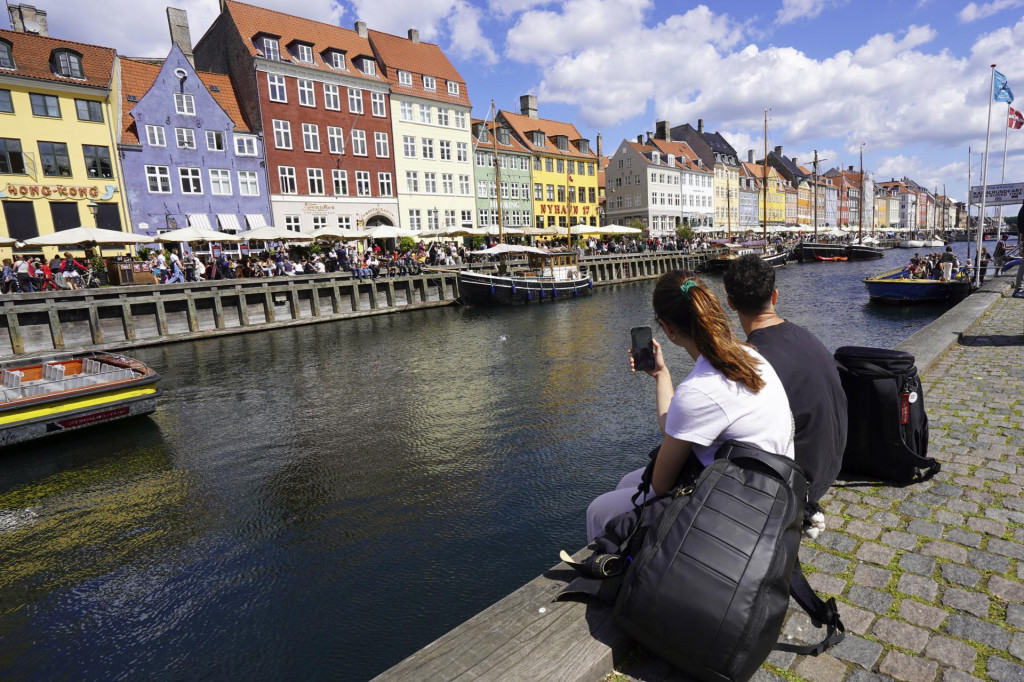 Turistka a turista sedia a sledujú vyhliadkové trajekty, ktoré sa plavia v historickej časti kodanského prístavu Nyhavn v dánskej metropole. FOTO: TASR/AP