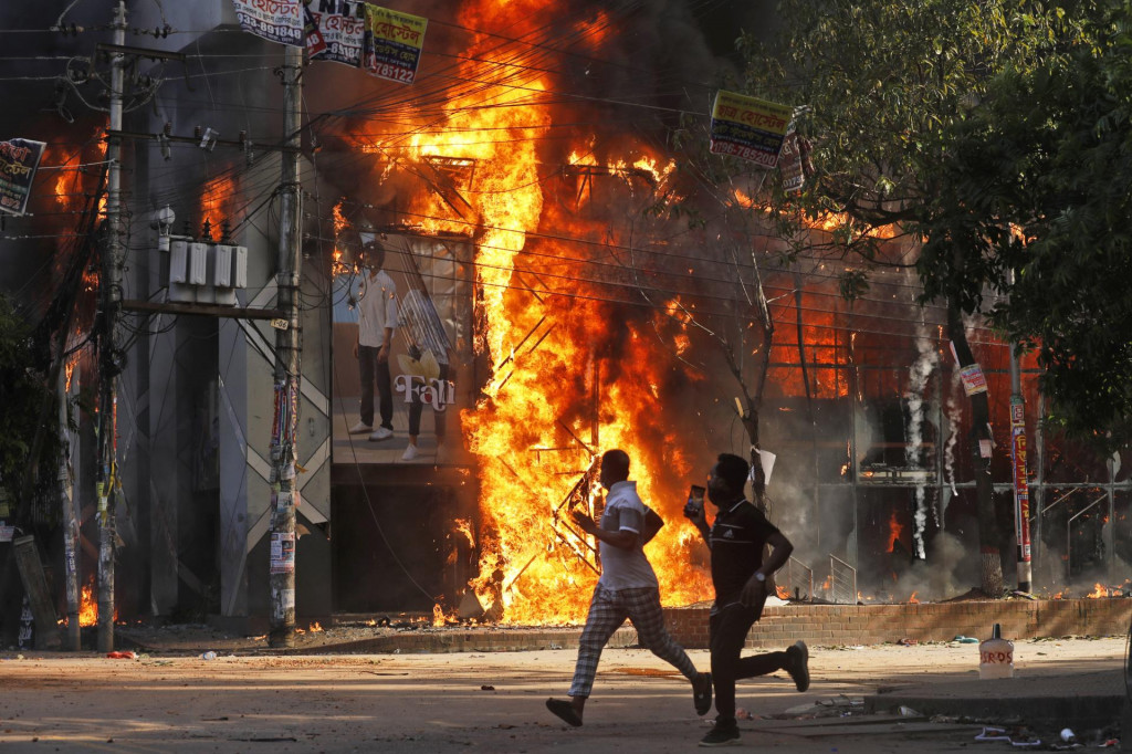 Muži bežia okolo horiaceho obchodu počas protivládneho protestu v bangladéšskej metropole Dháka. FOTO TASR/AP