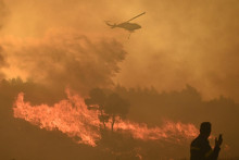 Hasičský vrtuľník zhadzuje vodu pri požiari v dedine Varnava neďaleko Atén v Grécku. FOTO: Reuters