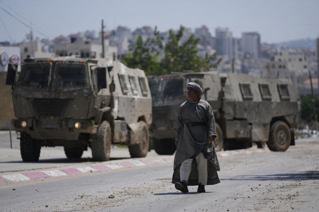 Palestínčan kráča okolo dvoch armádnych vozidiel počas razie izraelskej armády. FOTO: TASR/AP