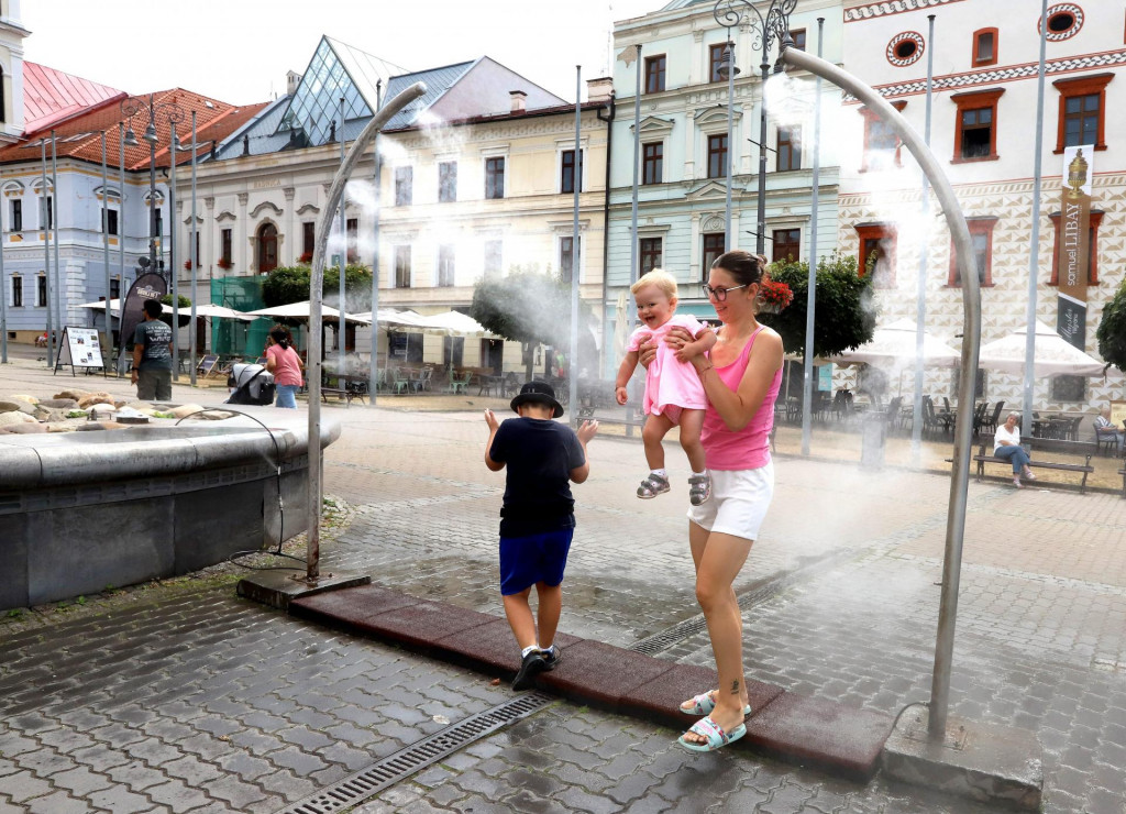 Na snímke ľudia prechádzajú cez vodný rozprašovač počas horúčav na Námestí SNP v Banskej Bystrici. FOTO: TASR/Ján Krošlák