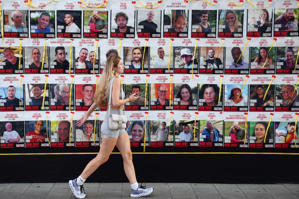 Žena kráča vedľa steny s plagátmi s rukojemníkmi unesenými Hamasom. FOTO: Reuters