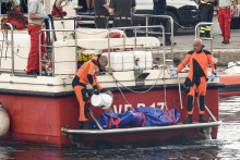 Talianski potápači vynášajú telo jednej z obetí potopenej plachetnice Bayesan v prístave v meste Porticello. FOTO: TASR/AP
