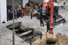 Záchranári používajú žeriav pri vyslobodzovaní ženy, ktorá spadla do jamy po prepadnutí chodníka následkom prudkých dažďov v malajzijskom Kuala Lumpure. FOTO: TASR/AP