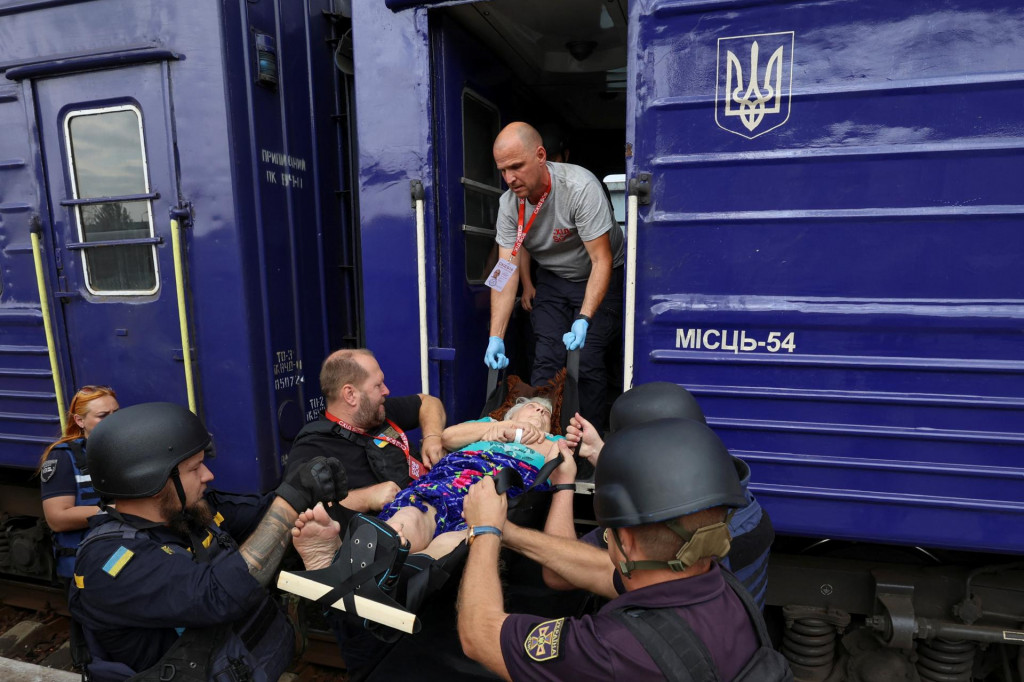 Dobrovoľníci a pohotovostní pracovníci nesú postihnutú ženu do evakuačného vlaku na západnú Ukrajinu v Pokrovsku. FOTO: Reuters