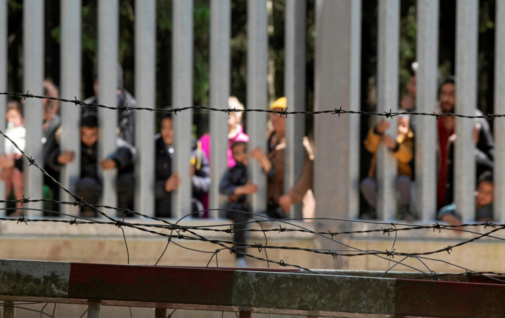 Migranti stoja pri múre na poľsko-bieloruskej hranici neďaleko poľského mesta Bialowieza. FOTO: REUTERS