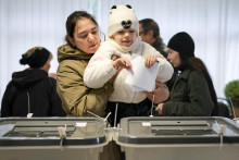 Žena drží dieťa, ktoré vhadzuje obálku do volebnej schránky v Kišiňove počas prezidentských volieb a referenda o začlenení Moldavska do Európskej únie. FOTO: TASR/AP