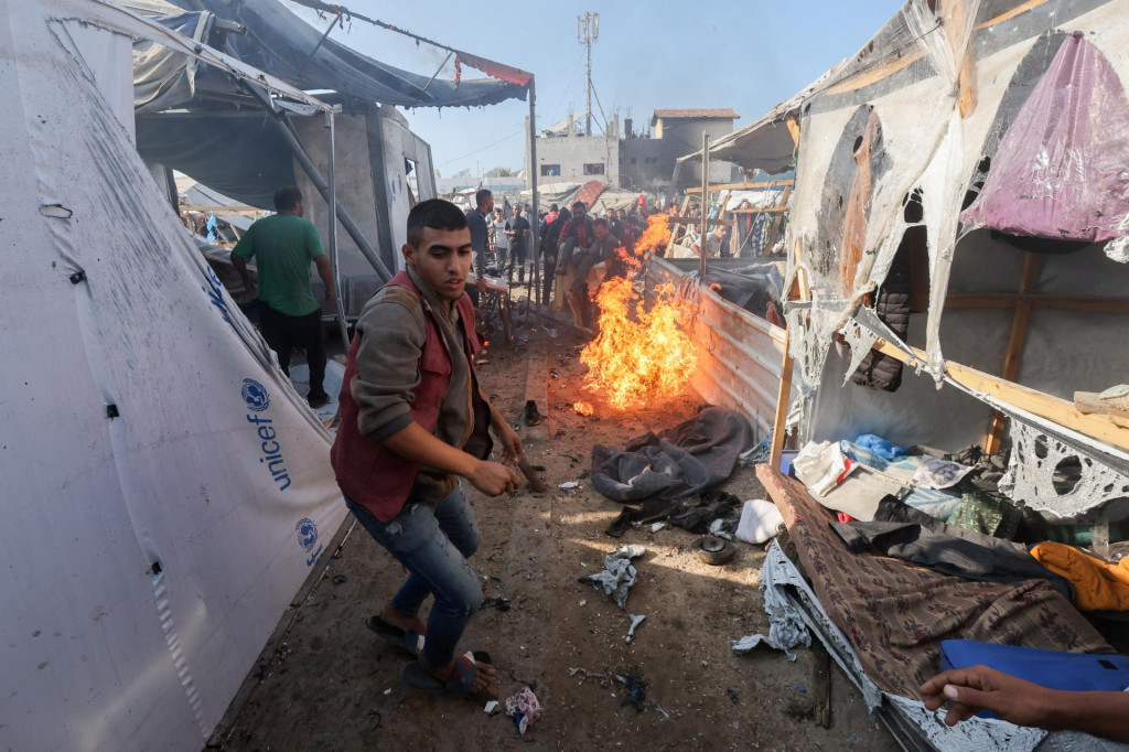 Muž stojí pri ohni, zatiaľ čo Palestínčania kontrolujú miesto izraelského útoku na stan, v ktorom sú presídlení ľudia v pásme Gazy. FOTO: Reuters