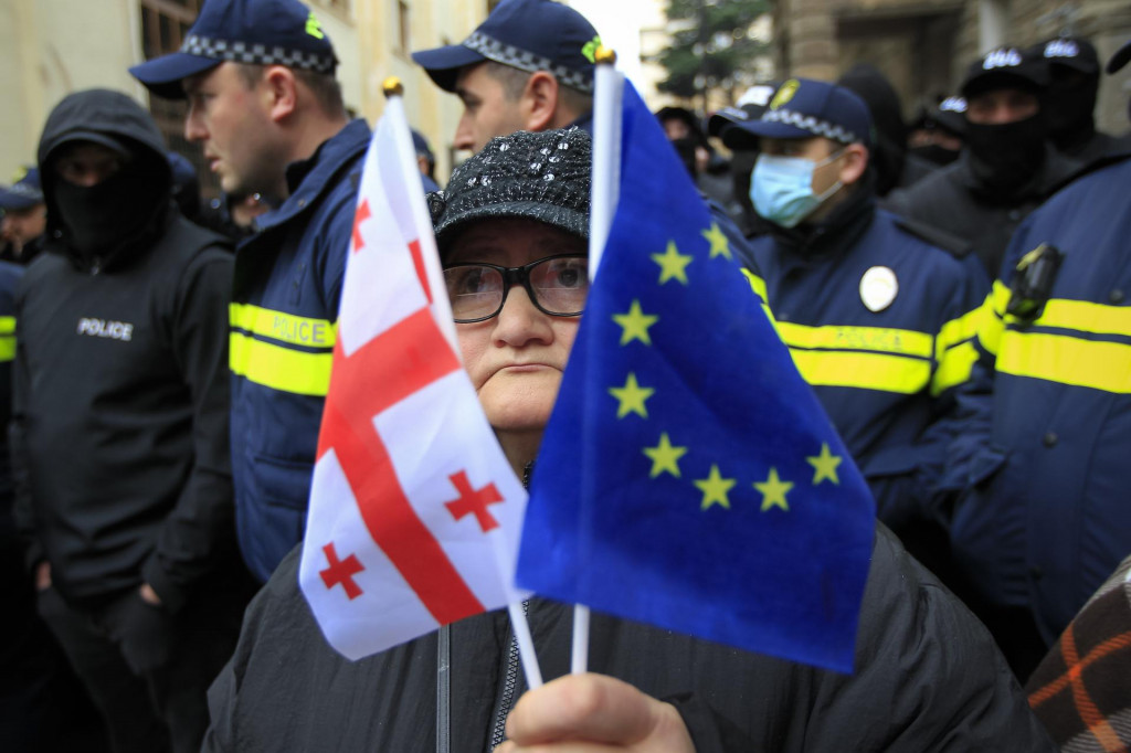 Žena s gruzínskou vlajkou a vlajkou Európskej únie stojí pred policajtami počas zhromaždenia demonštrantov, ktorí požadujú nové parlamentné voľby v Gruzínsku, neďaleko budovy parlamentu v Tbilisi. FOTO: TASR/AP