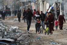 Palestínčania kráčajú po zničenej ulici. FOTO: Reuters