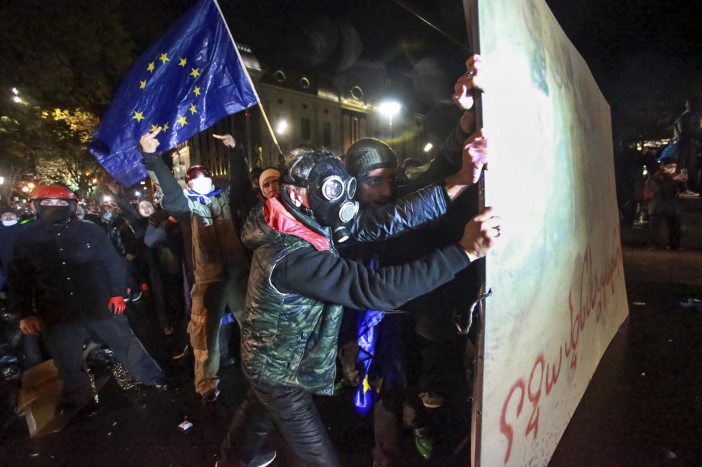 Demonštrant s plynovou maskou na tvári sa chráni časťou plota pred vodným delom, ktoré použila polícia počas masových protestov pred budovu parlamentu v Tbilisi. FOTO: TASR/AP