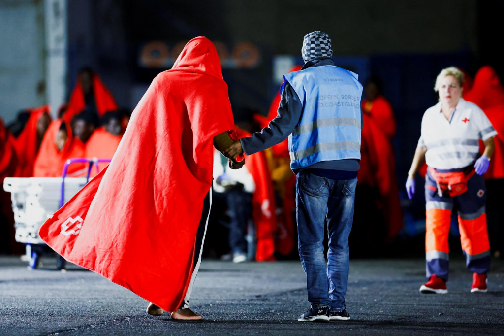 Člen Európskej pohraničnej a pobrežnej stráže Frontex pomáha migrantovi po vylodení z plavidla španielskej pobrežnej stráže v prístave Arguineguin na Kanárskych ostrovoch. FOTO: Reuters