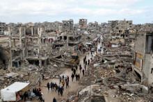 Palestínčania prechádzajú popri troskách budov zničených počas izraelskej ofenzívy v meste Gaza. FOTO: Reuters