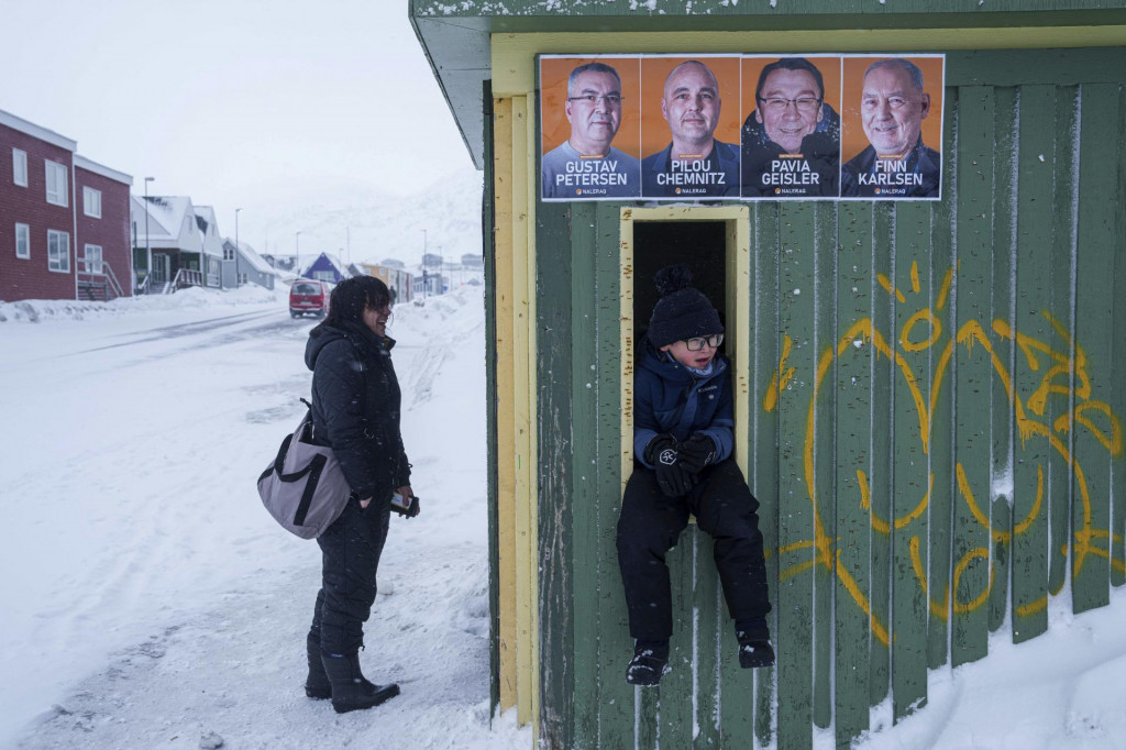 Chlapec sedí na autobusovej zastávke, na ktorej sú polepené plagáty politikov v grónskej metropole Nuuk pred parlamentnými voľbami v Grónsku. FOTO: TASR/AP