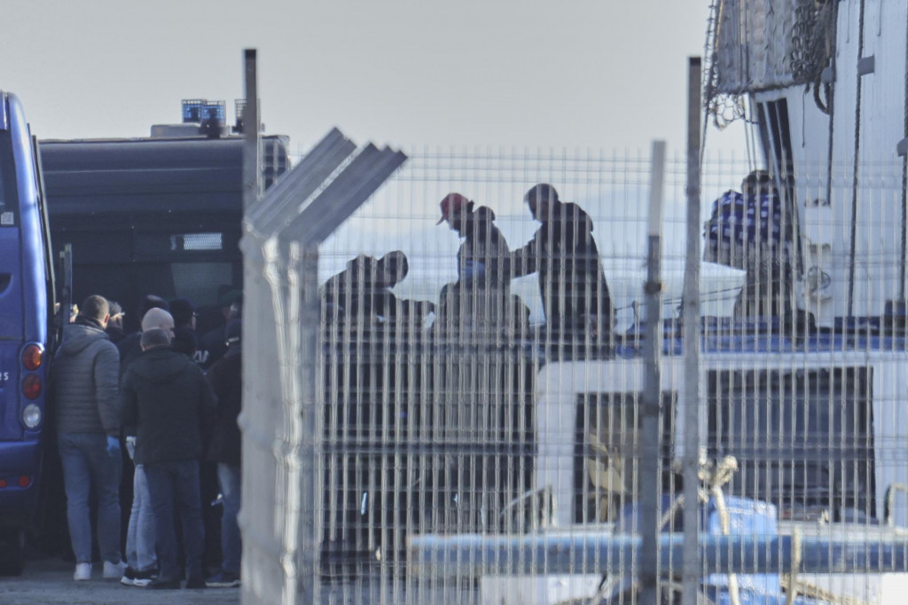 Migrant v sprievode policajtov vystupuje z lode talianskeho námorníctva. FOTO: TASR/AP