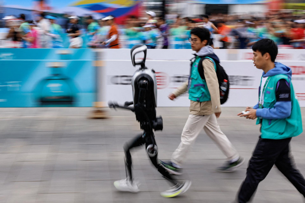Inžinieri bežia s humanoidným robotom Kuavo, ktorý sa spolu s ľudskými bežcami zúčastňuje polmaratónu E-Town a polmaratónu humanoidných robotov v Pekingu, Čína 19. apríla 2025. FOTO: REUTERS