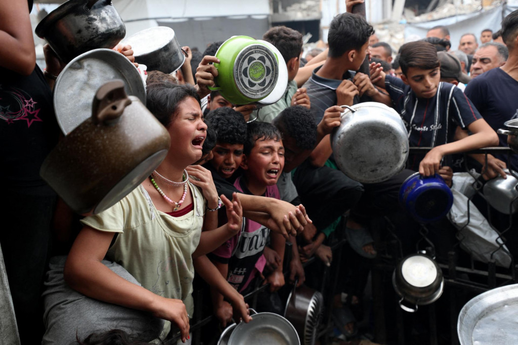 Deti reagujú, keď Palestínčania čakajú na jedlo pripravené charitatívnou kuchyňou v Beit Lahia v severnom pásme Gazy 24. apríla 2025. FOTO: REUTERS