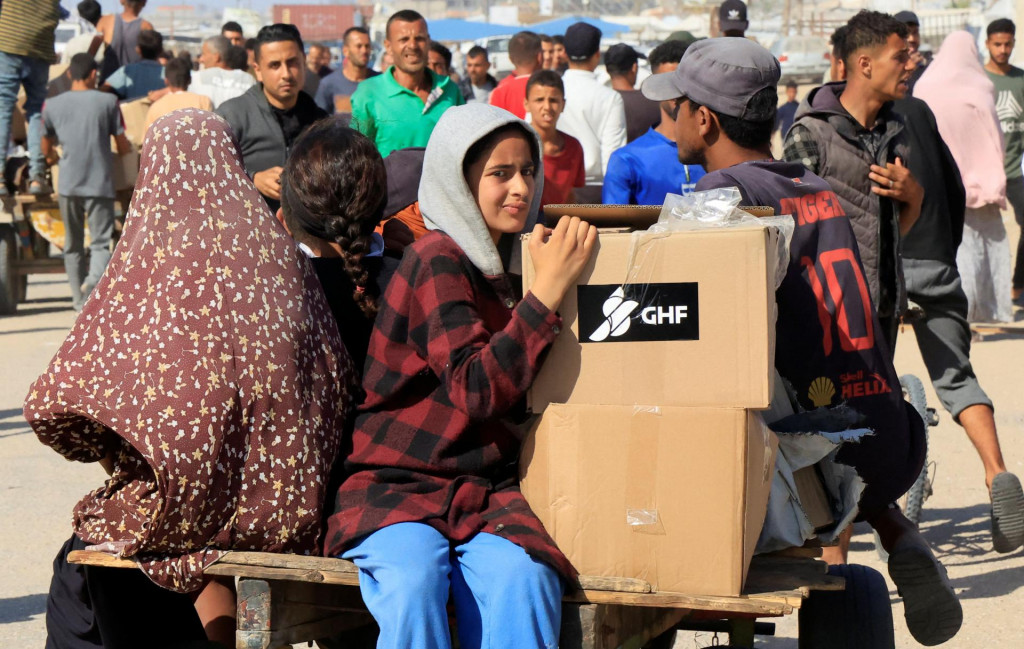 Ľudia sa veziu na vozíku, zatiaľ čo sa Palestínčania hľadajúci pomoc zhromažďujú neďaleko miesta distribúcie pomoci, ktoré prevádzkuje Humanitárna nadácia pre Gazu podporovaná USA, v Rafahu v južnom pásme Gazy. FOTO: REUTERS