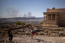 Turista pózuje na fotografii na vrchole Akropoly, zatiaľ čo v pozadí horí lesný požiar uprostred vysokých teplôt v Aténach v Grécku 16. júla 2024. FOTO: REUTERS