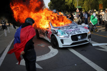 Demonštrant zahalený vo vlajke Samoy stojí pri horiacom aute počas protestu proti federálnym imigračným raziám v centre Los Angeles. FOTO: Reuters