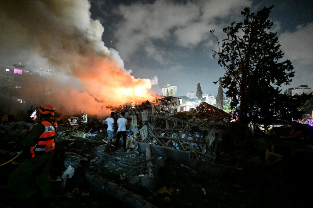 Miestni obyvatelia pozerajú na požiar na mieste dopadu rakety po raketovom útoku z Iránu na Izrael v centrálnom Izraeli 15. júna 2025. FOTO: REUTERS