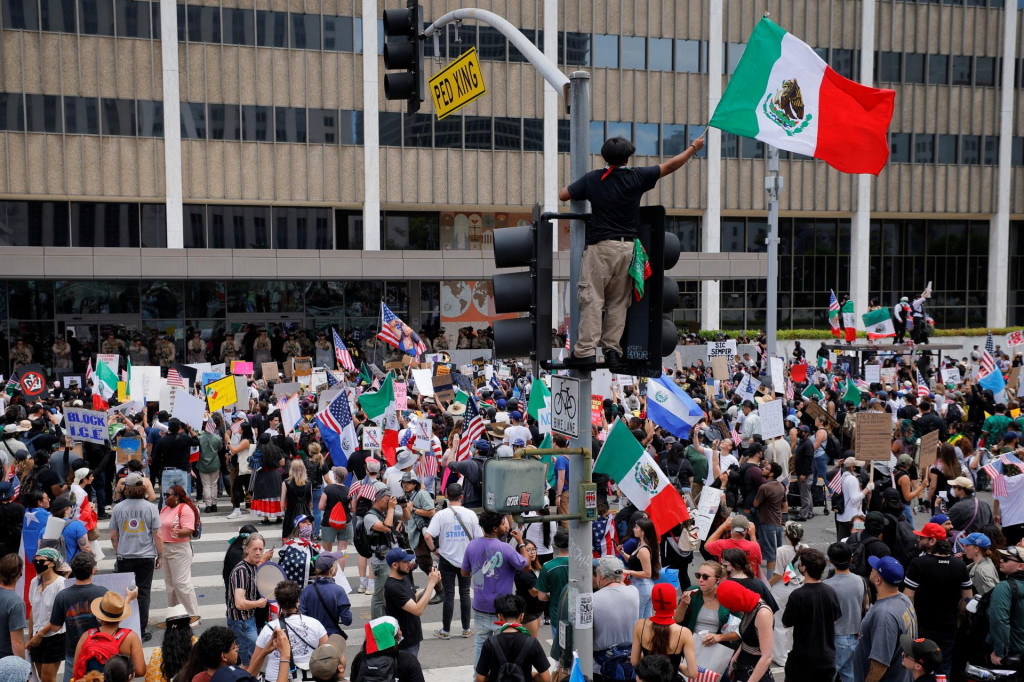 Demonštrant máva mexickou vlajkou, zatiaľ čo americkí mariňáci stoja na stráži pred federálnou budovou Edwarda R. Roybala počas protestu v Los Angeles. FOTO: Reuuters