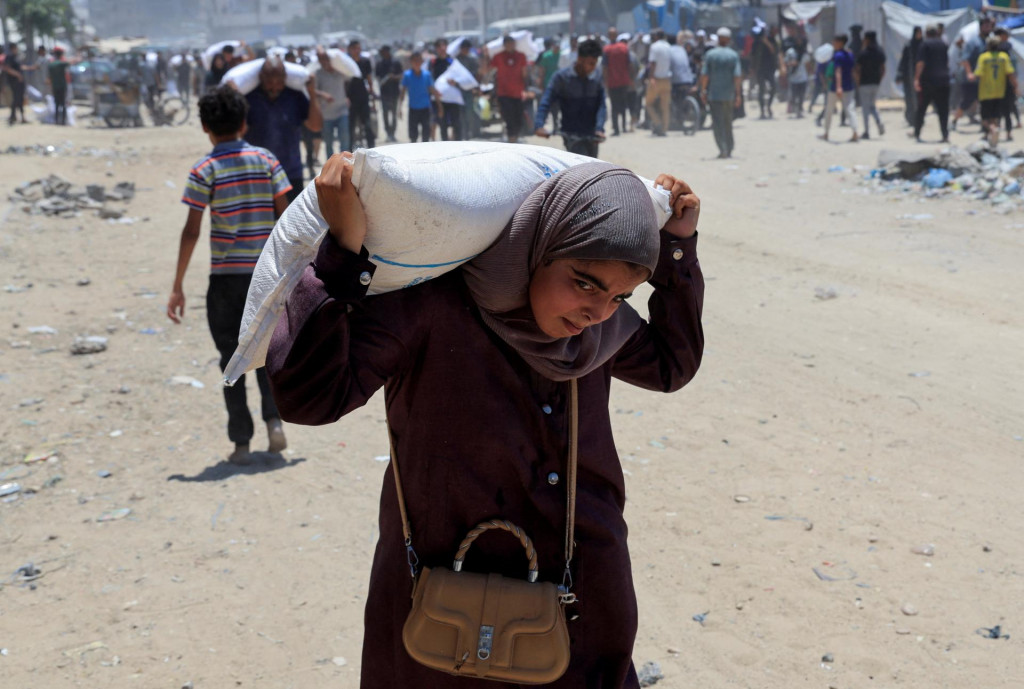Palestínčan nesie vrece múky, zatiaľ čo sa ľudia zhromažďujú, aby si prevzali pomoc v Chán Júnis v južnom Pásme Gazy. FOTO: Reuters