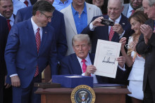 Americký prezident Donald Trump obklopený desiatkami republikánskych poslancov ukazuje podpísaný zákon o daňových a výdavkových škrtoch v Bielom dome vo Washingtone.  FOTO: TASR/AP