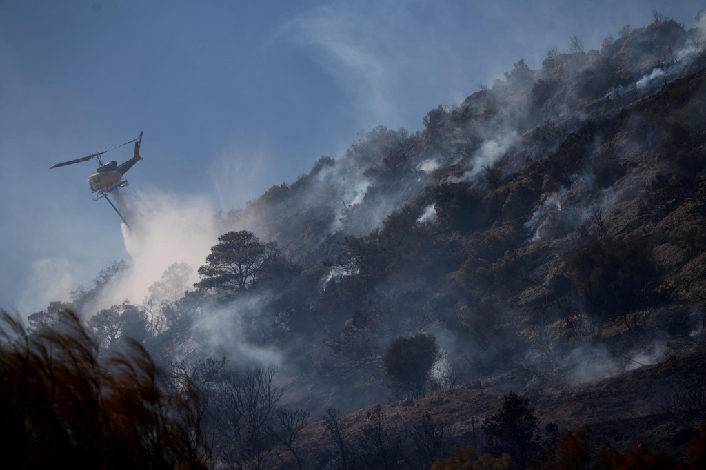 Hasičský vrtuľník zasahuje počas lesného požiaru v meste Koropi neďaleko Atén. FOTO: Reuters