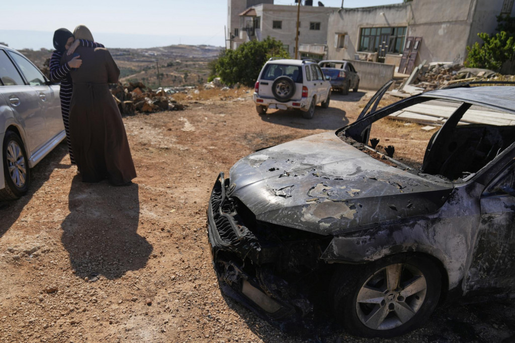 Ženy sa utešujú pri obhorenom aute po nočnom útoku izraelských osadníkov v židovskej osade Kufr Malek na Západnom brehu Jordánu, východne od Ramalláhu. FOTO: TASR/AP