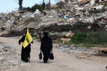 Ženy kráčajú okolo zničených budov, jedna z nich drží vlajku Hizballáhu, v juholibanonskej dedine Kfar Kila. FOTO: Reuters