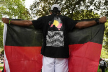 Muž drží vlajku na proteste domorodých Austrálčanov počas Dňa Austrálie v Sydney (26. januára 2024). FOTO: TASR/AP