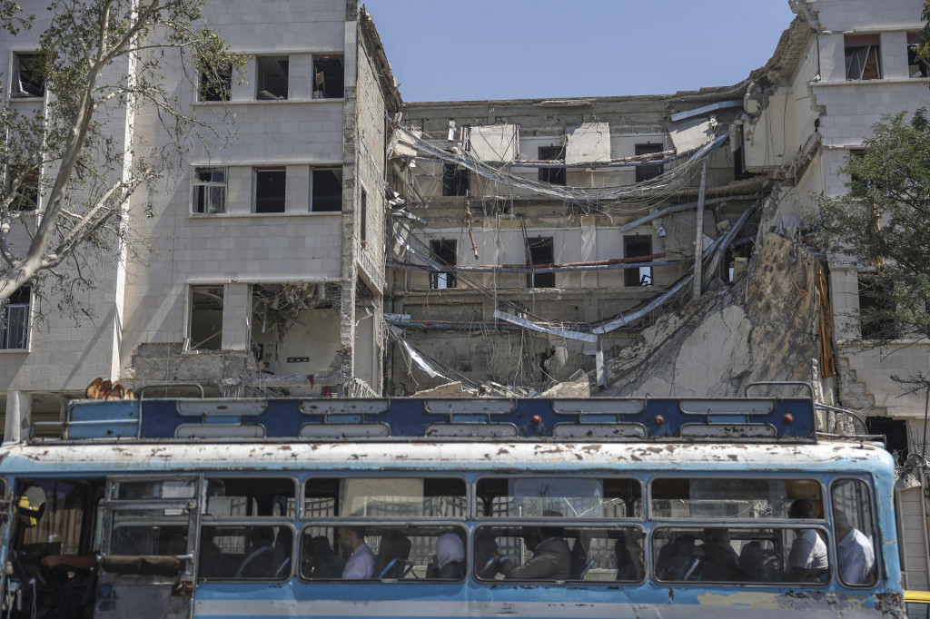 Ľudia sedia v autobuse, ktorý prechádza okolo zničenej budovy sýrskeho ministerstva obrany po izraelských náletoch v sýrskom Damasku 17. júla 2025. FOTO: TASR/AP