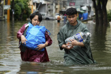 Obyvatelia nesú veci a pitnú vodu pri brodení sa cez zaplavenú ulicu po záplavách spôsobených prudkým monzúnovým dažďom v meste Cainta vo filipínskej provincii Rizal, na juhozápade Filipín 23. júla 2025. FOTO: TASR/AP