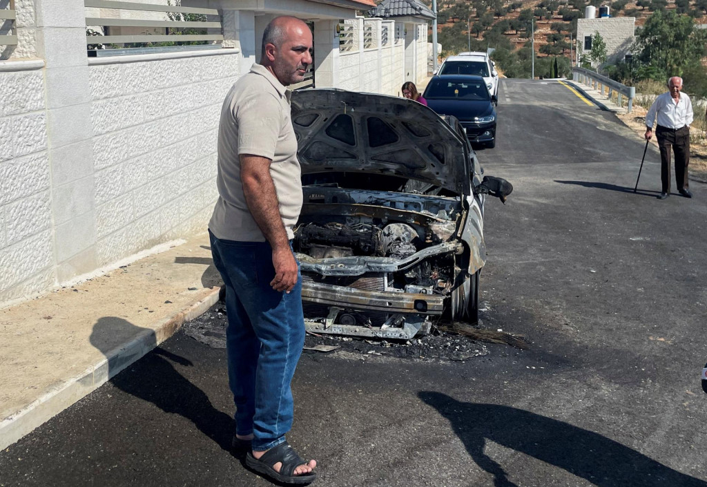 Palestínčan stojaci pri zapálenom aute v dedine Tajba. FOTO: REUTERS