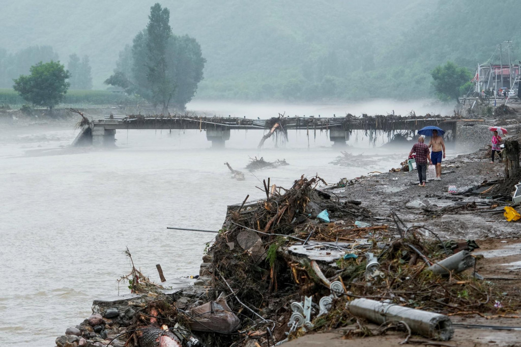 Ľudia prechádzajú okolo poškodeného mosta po silných dažďoch, ktoré zaplavili Peking. FOTO: Reuters