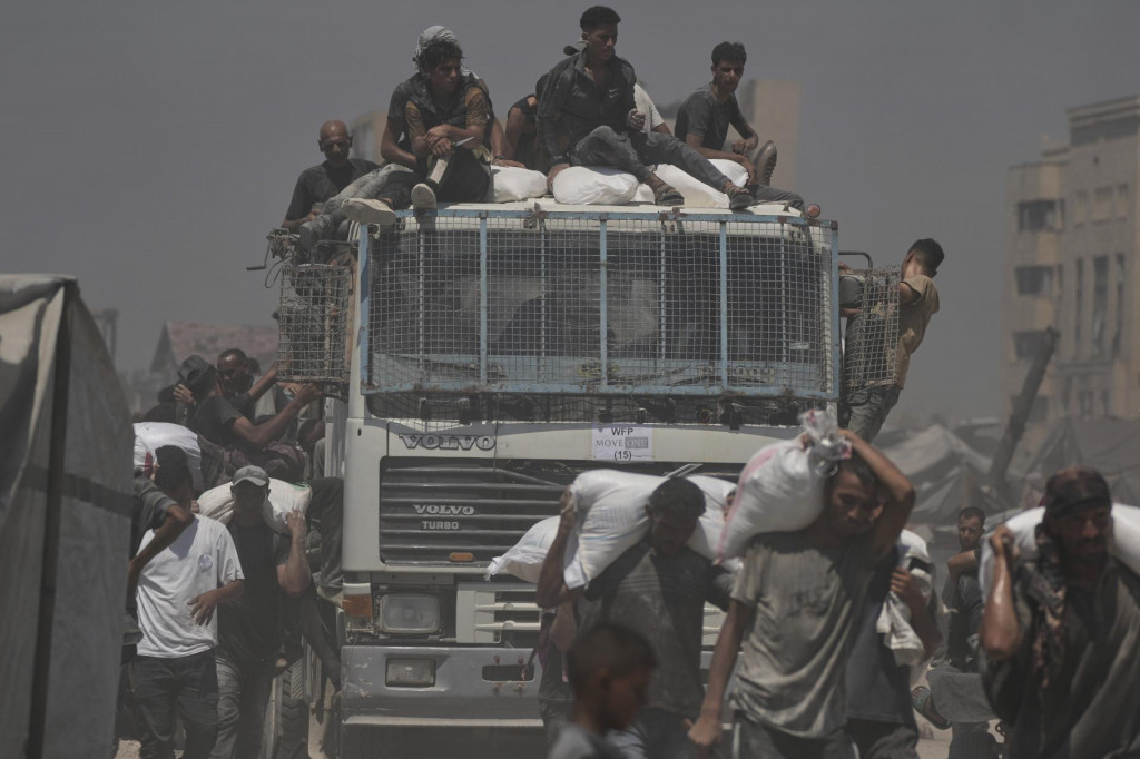 WA 46 Gaza - Palestínčania si odnášajú vrecia s múkou, ktoré priviezli kamióny s humanitárnou pomocou do mesta Gaza. FOTO: TASR/AP