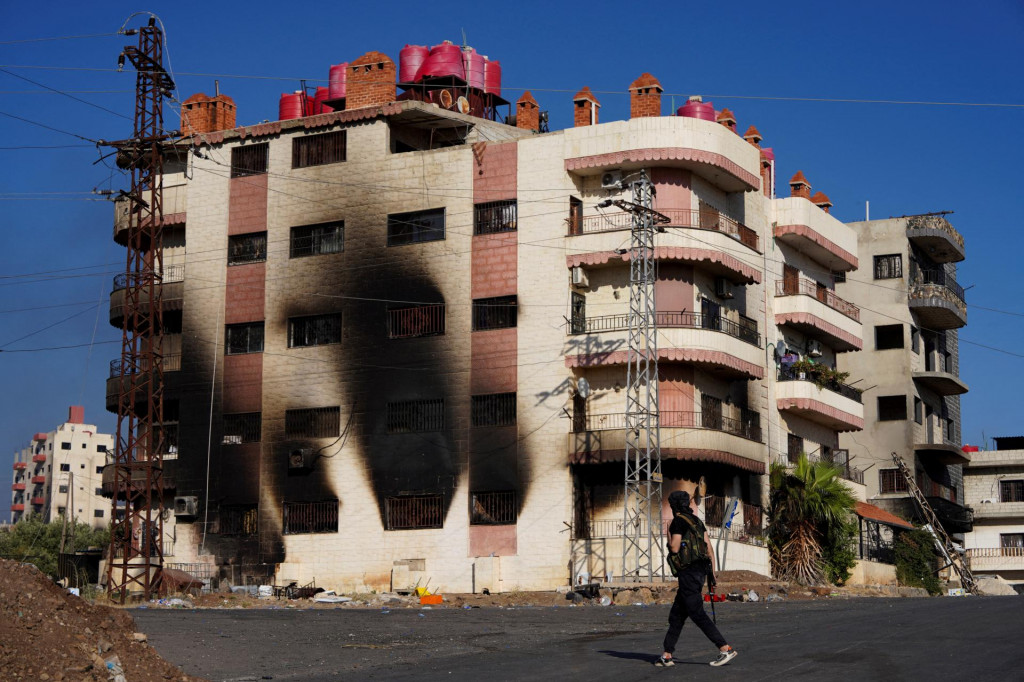 Beduínsky bojovník sa prechádza blízko vyhorenej budovy v juhosýrskej provincii Suwajdá. FOTO: Reuters