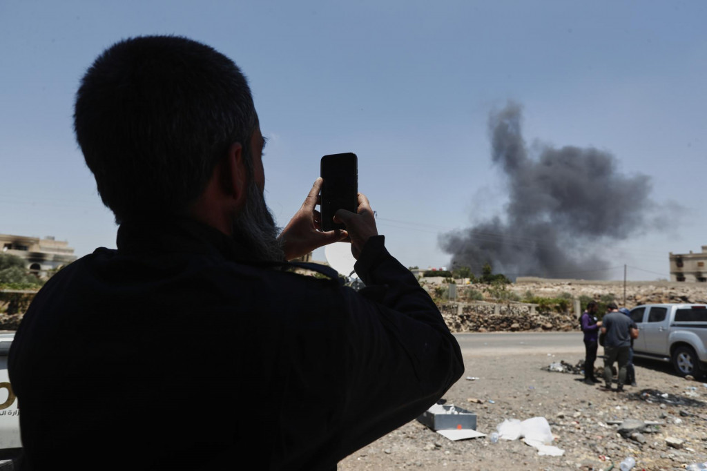 Príslušník sýrskych bezpečnostných síl si filmuje na mobil stúpajúci dym z horiacich domov v dedine Mazrá, na predmestí mesta Suwajdá na juhu Sýrie. FOTO: TASR/AP