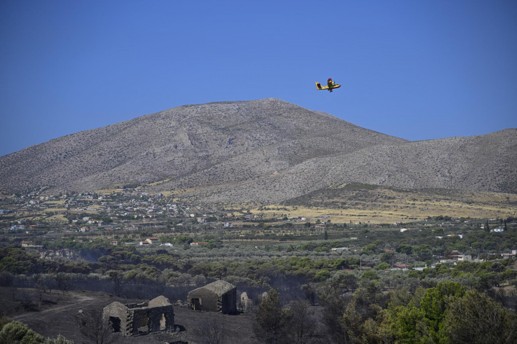 Hasičské lietadlo letí nad zhorenou oblasťou po lesnom požiari v dedine Charvalo, juhovýchodne od Atén. FOTO: TASR/AP