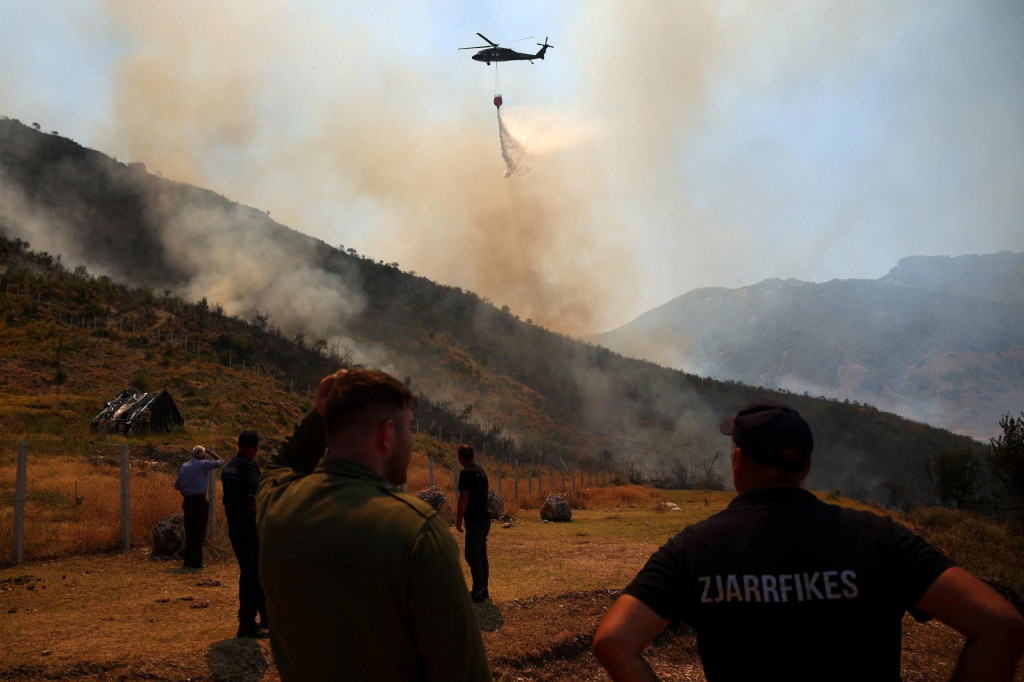 Príslušníci záchranných zložiek a miestni obyvatelia sledujú, ako slovenský vrtuľník zhadzuje vodu na lesný požiar neďaleko Tepeleny v Albánsku. FOTO: REUTERS
