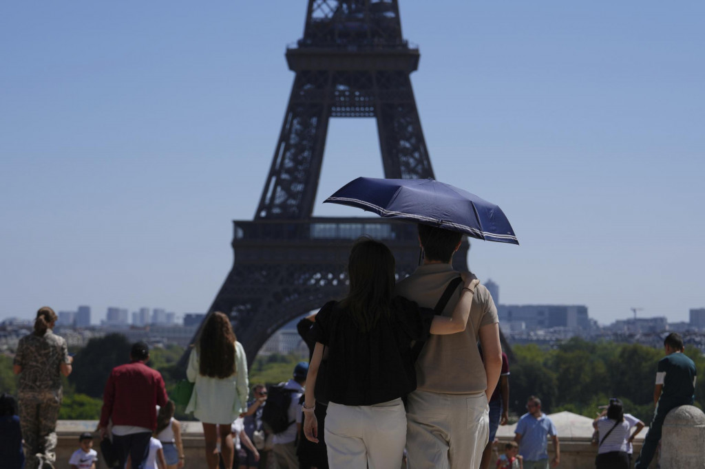 Turisti sa chránia pred Eiffelovou vežou dáždnikom počas horúčav v Paríži. FOTO: TASR/AP
