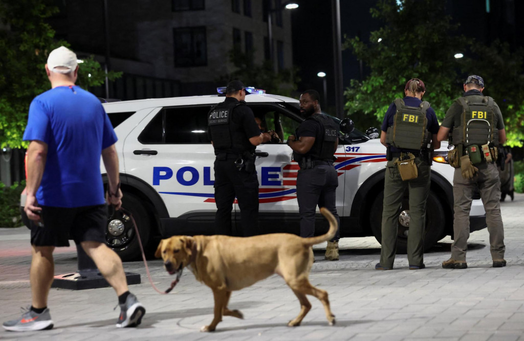 Muž sa prechádza so psom, zatiaľ čo agenti FBI a príslušníci tajnej služby hliadkujú v štvrti Navy Yard po oznámení prezidenta USA Donalda Trumpa o nasadení Národnej gardy a federalizácii Metropolitného policajného oddelenia vo Washingtone. FOTO: Reuters